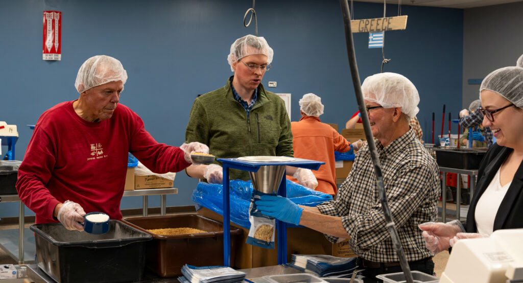Emily Peterson and Brandon Hebert from Perspective 6 Group pictured with two clients portioning out ingredients and filling meal packs at Feed My Starving Children.