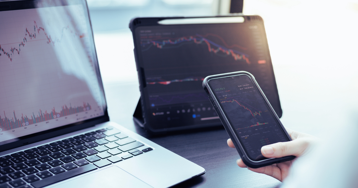 Photograph of someone holding a phone with a tablet and computer up all monitoring the stock market to illustrate the need for sound advice in regards to non-qualified stock options taxation.