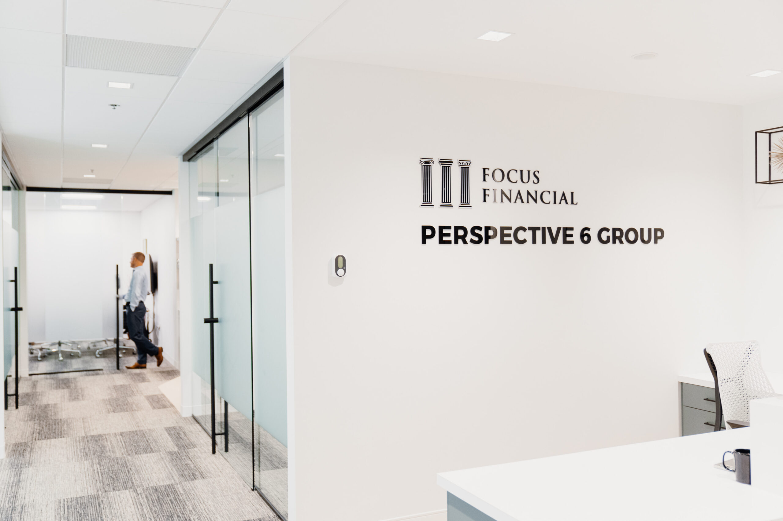 Photograph of Partner, Matthew Finley, standing down the hall in a doorway with Perspective 6 Group's logo on the wall in the foreground to illustrate the journey of Perspective 6 Group.